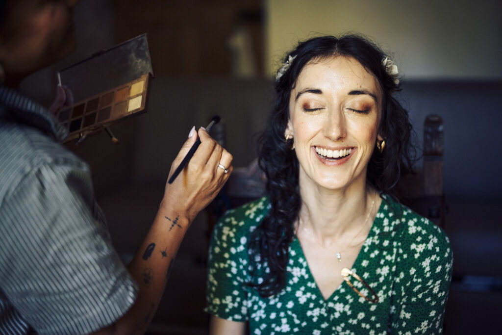La mariée rit pendant qu'elle se fait maquiller au Domaine le Taleur à Avignon, capturant un moment spontané et joyeux des préparatifs.